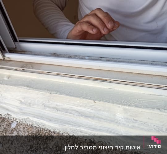 אדם מורח חומר איטום על מסגרת חלון